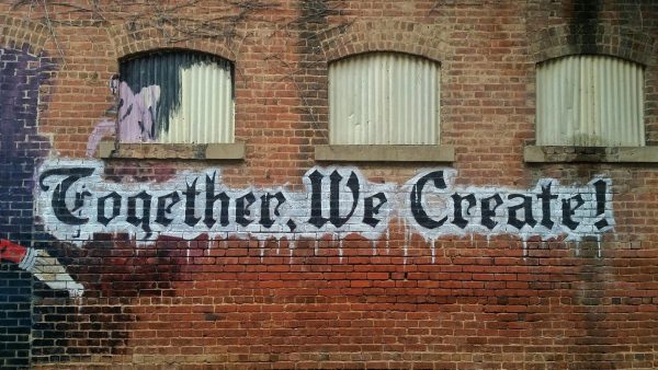 A brick wall, marked with a graffiti that says ''Together We Create!''
